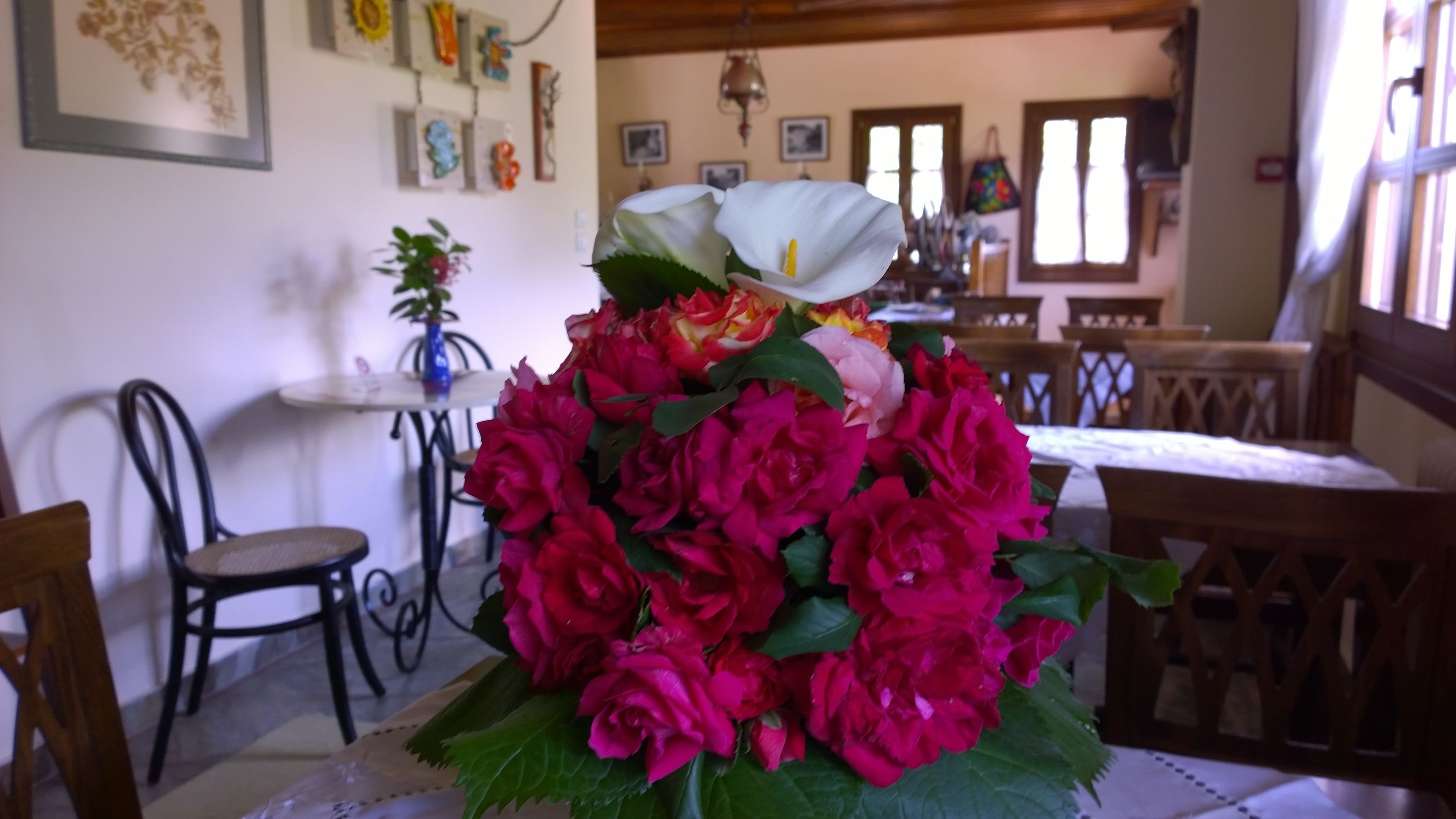 A dining area with a table set for two, surrounded by wooden chairs. A vase with a bouquet of red roses is prominently displayed in the center.