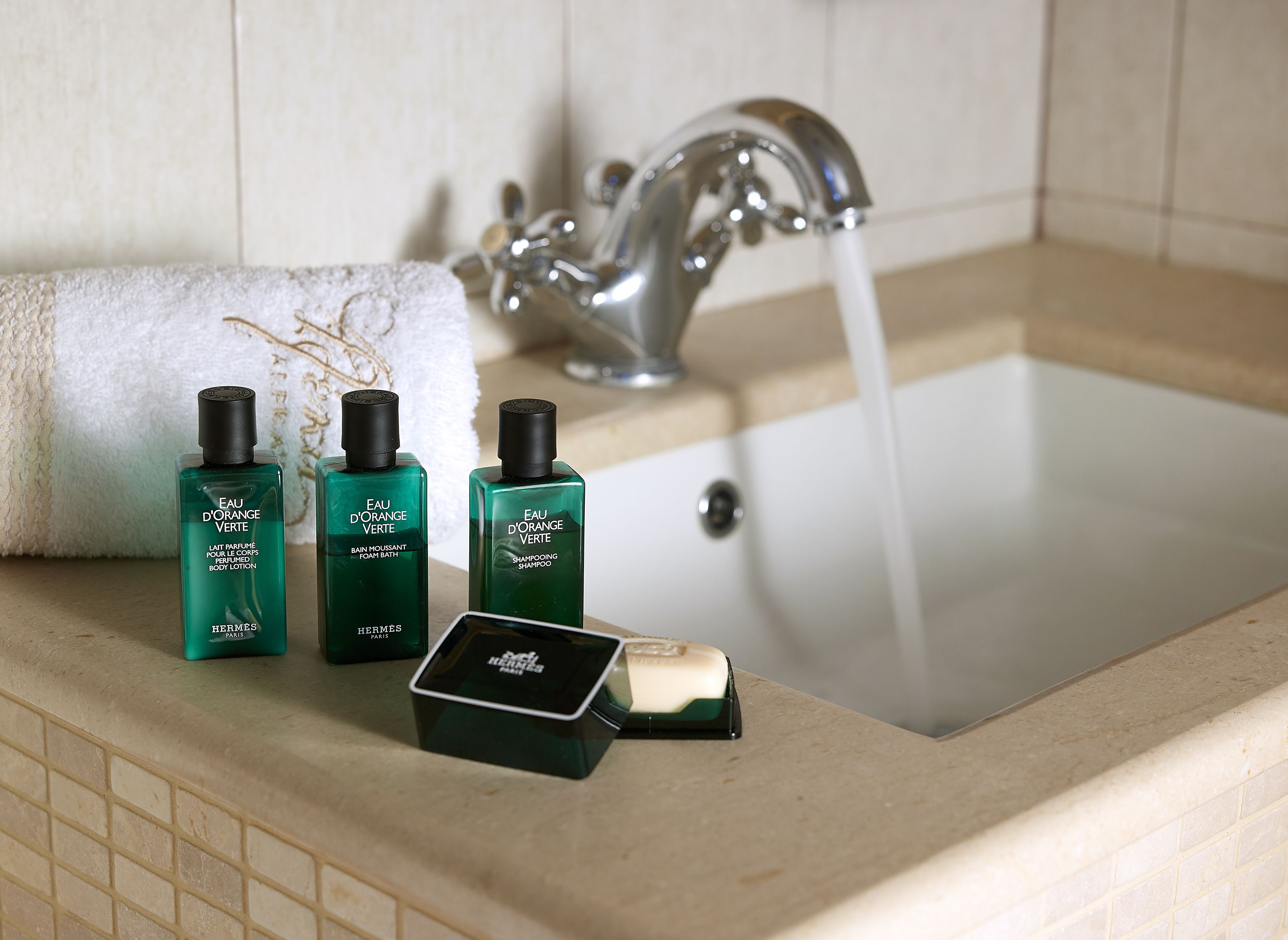 A bathroom sink with three bottles of Eau d'Orange Verte body lotion, a bar of soap, and a towel.