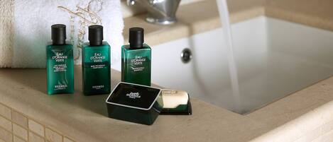 Un lavamanos con tres botellas de loción corporal Eau d'Orange Verte, una barra de jabón y una toalla.