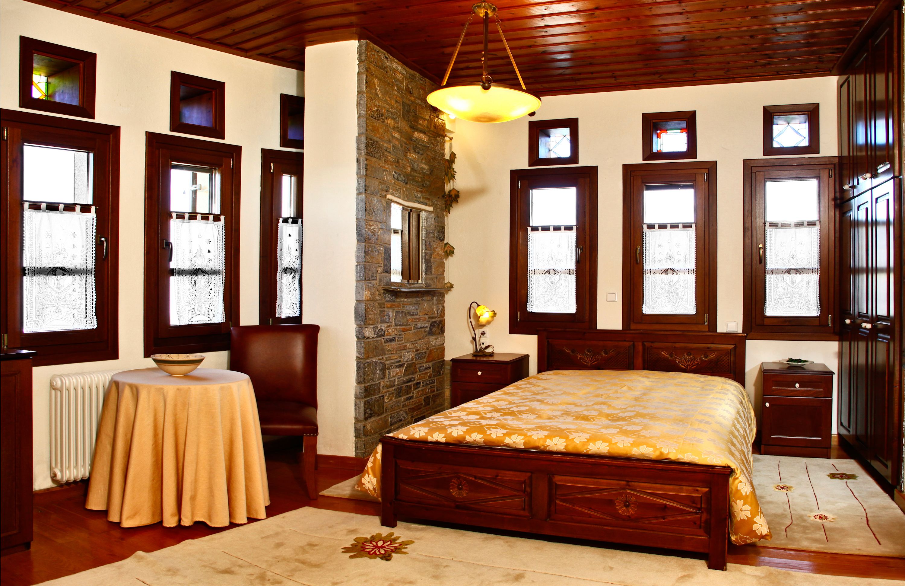 Un dormitorio con una cama grande, techo de madera, pared de piedra y varias ventanas.
