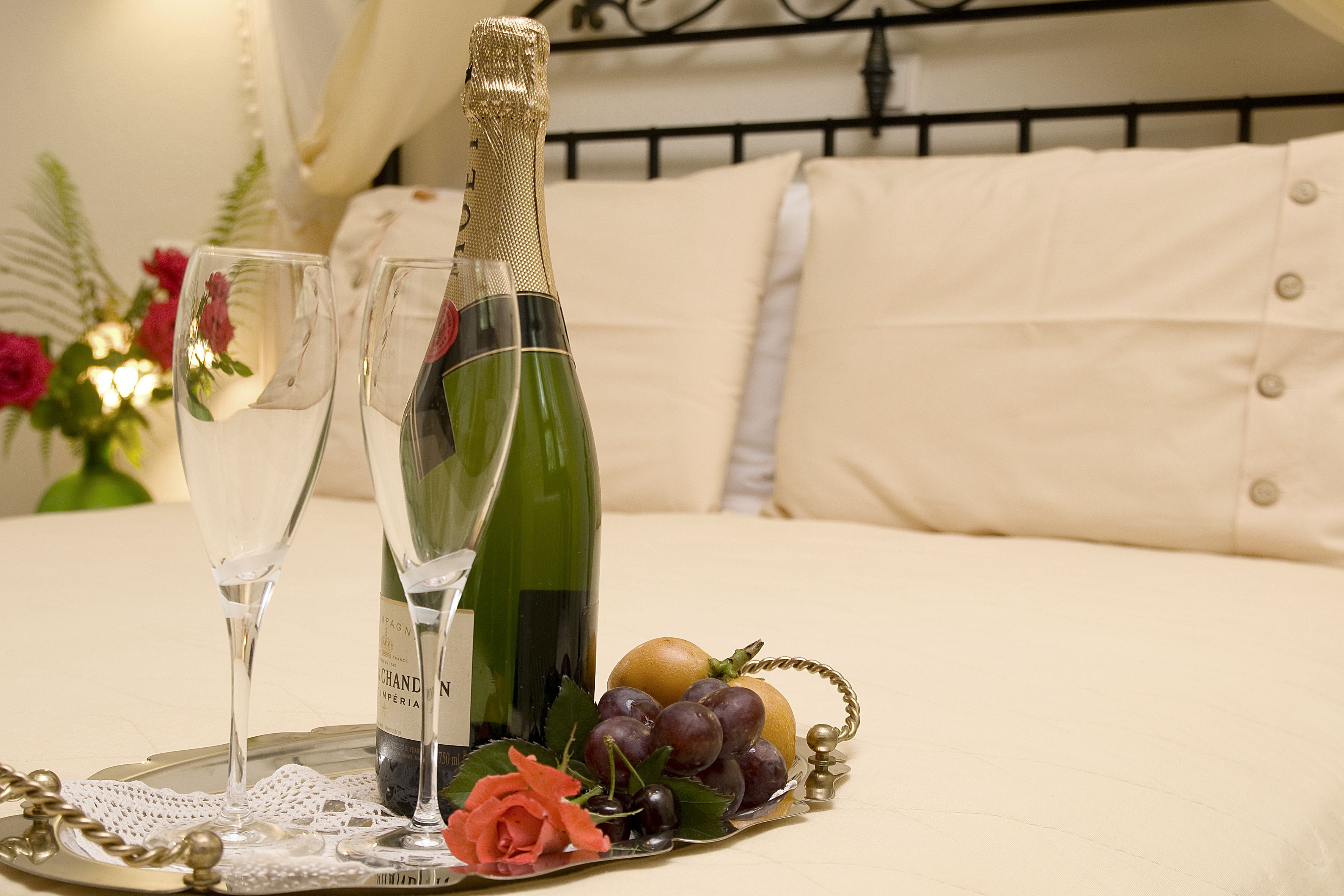 Una cama con estructura metálica, una botella de champán, dos copas y una bandeja con uvas y una rosa.