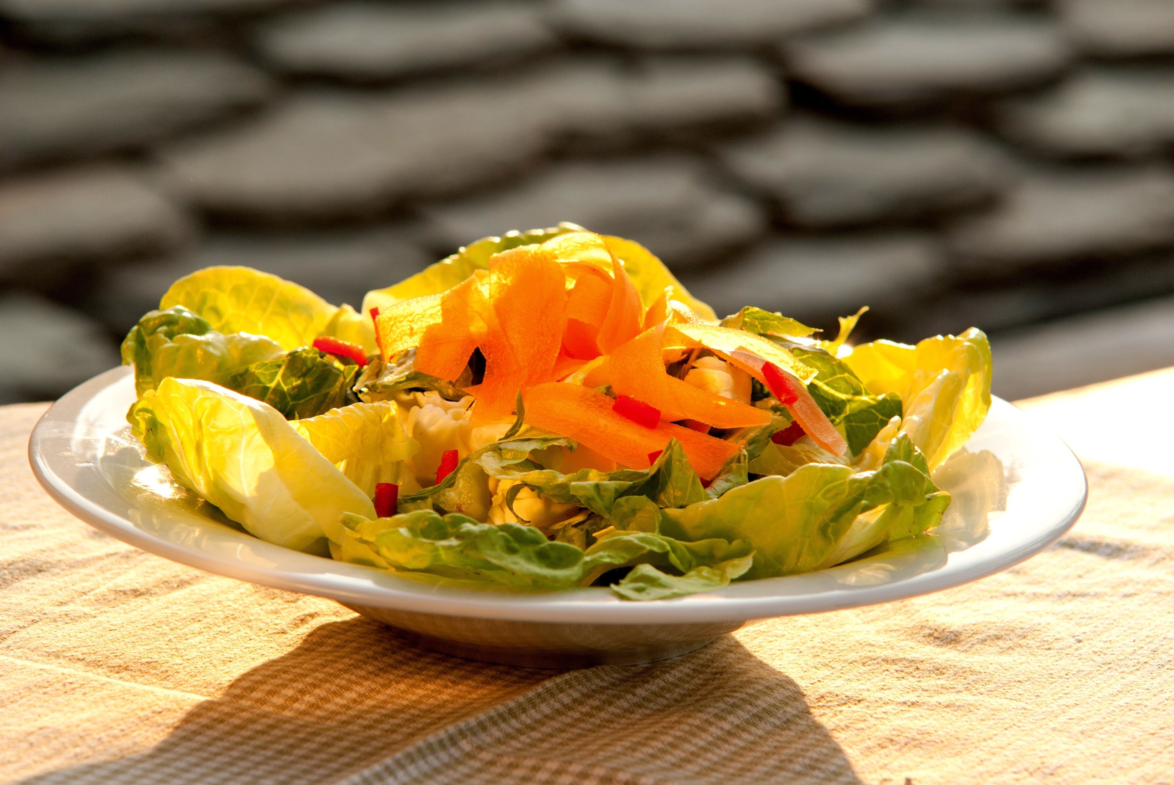 A plate of salad with lettuce and carrots on a tablecloth.
