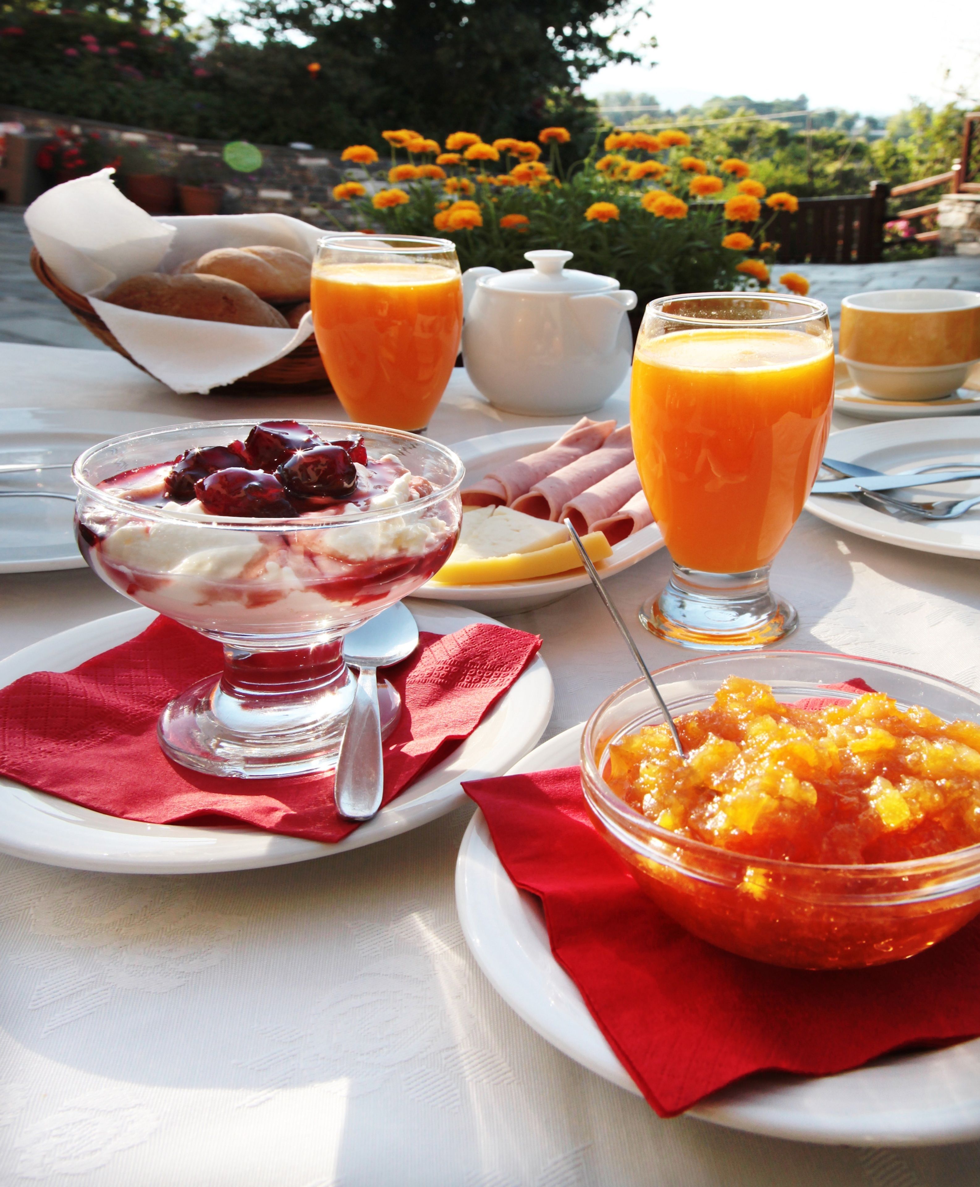Un desayuno con diferentes platos, como un bol de fruta, un vaso de zumo de naranja y un plato con jamón y queso en lonchas.