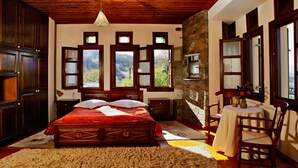 A bedroom with a large bed, wooden furniture, a stone wall, and multiple windows. - Aleka's House (Zagora-Mouresi)
