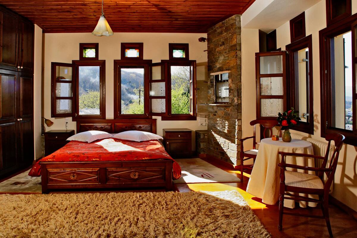 Un dormitorio con una cama grande, muebles de madera, una pared de piedra y varias ventanas.