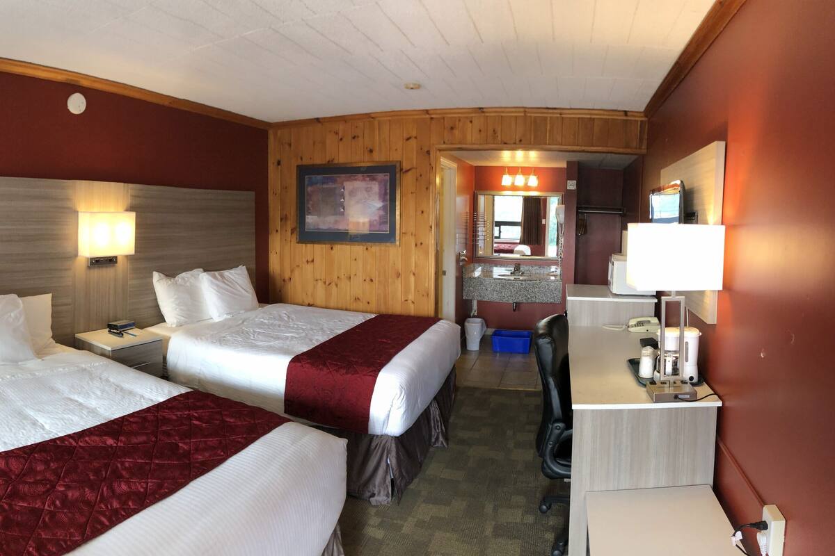 Une chambre d’hôtel avec deux lits, un bureau, un miroir et une salle de bain visible à travers une porte ouverte.