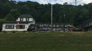 A motel with a green roof, a flag, and a parking lot with cars. - Knights Inn Huntsville, ON (Huntsville)