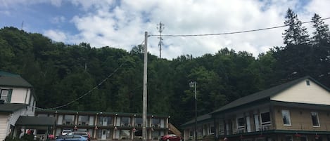 Un motel de dos pisos, con estacionamiento y un bosque al fondo.