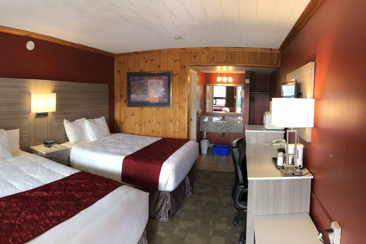 Une chambre d’hôtel avec deux lits, un bureau, une chaise, un lavabo et un miroir.