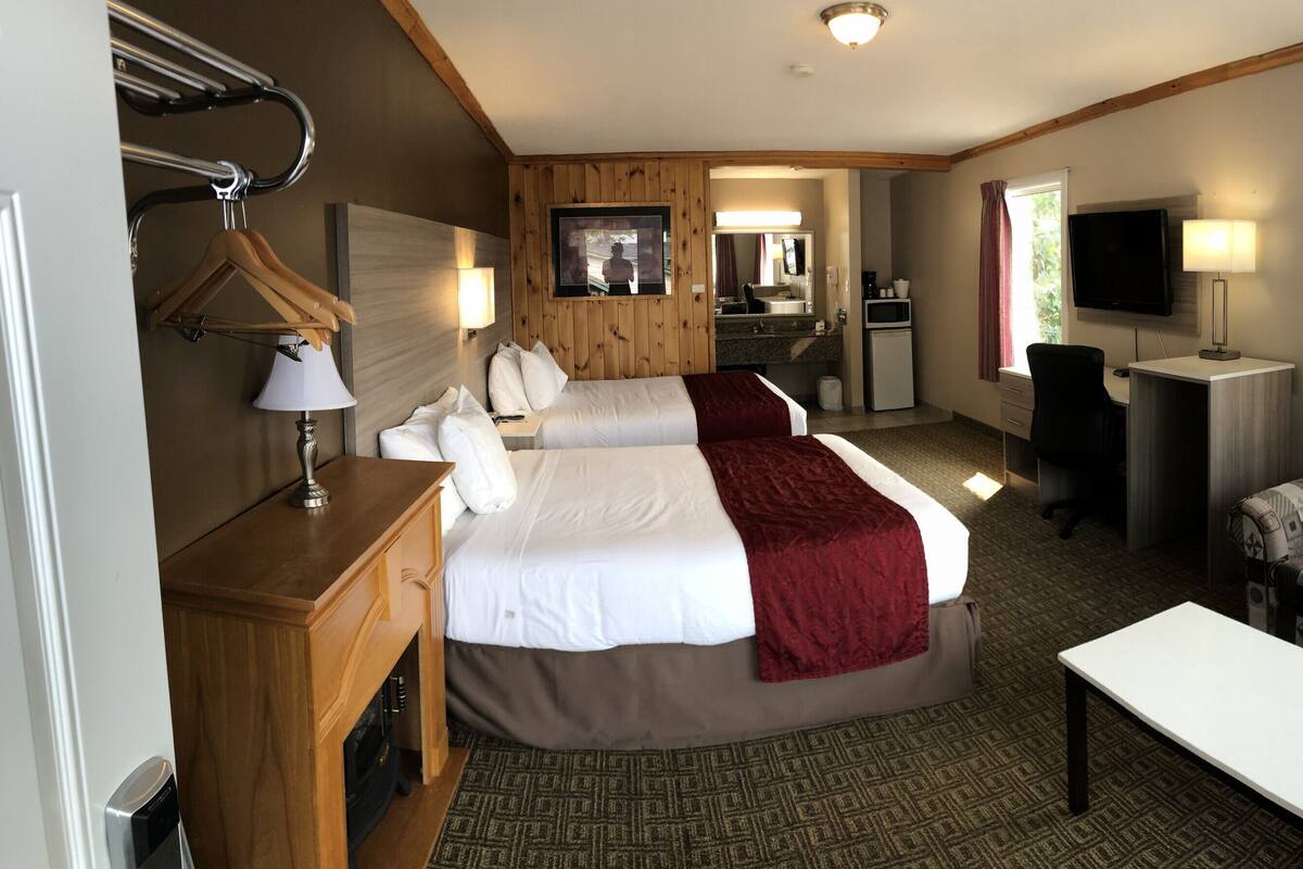 Une chambre d’hôtel avec deux lits, un bureau, une chaise, une télévision et une petite kitchenette.