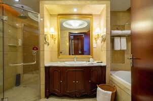 Un baño con cabina de ducha de vidrio, tocador con espejo grande y apliques de pared, bañera y perchero para toallas.