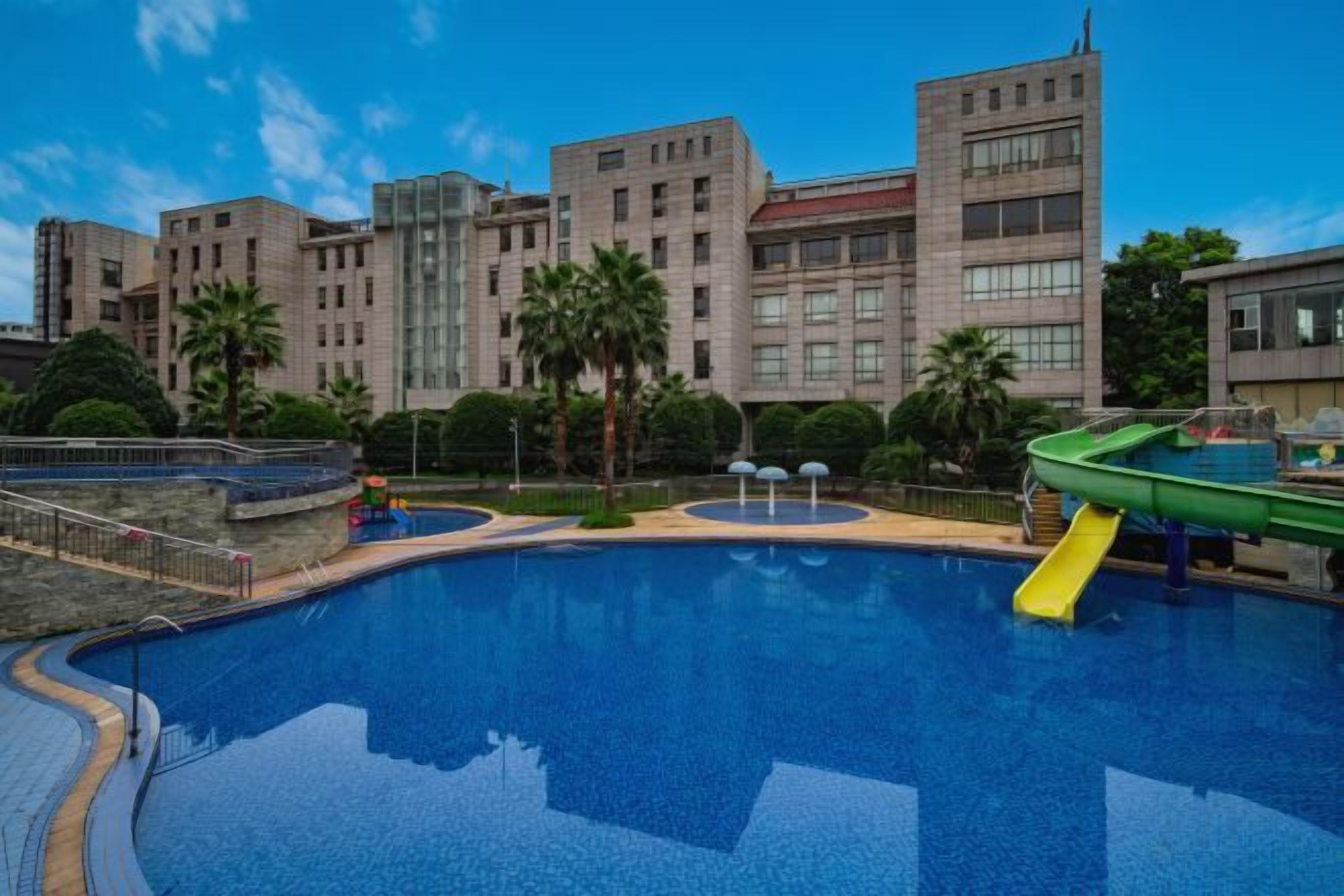 Una piscina con uno scivolo, circondata da edifici e palme.