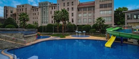 A swimming pool with a slide, surrounded by buildings and palm trees.