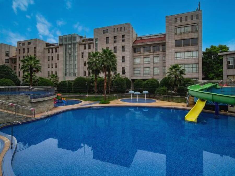 A swimming pool with a slide, surrounded by buildings and palm trees.