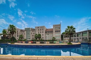 Un hotel moderno con piscina rodeada de palmeras y un cielo azul despejado.