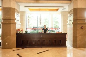 A reception desk with a receptionist, large windows, and a view of a car outside. - Xintian International Hotel (Xiangtan)