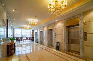 Un vestíbulo de hotel con piso de mármol, candelabros, ascensores y una recepción.