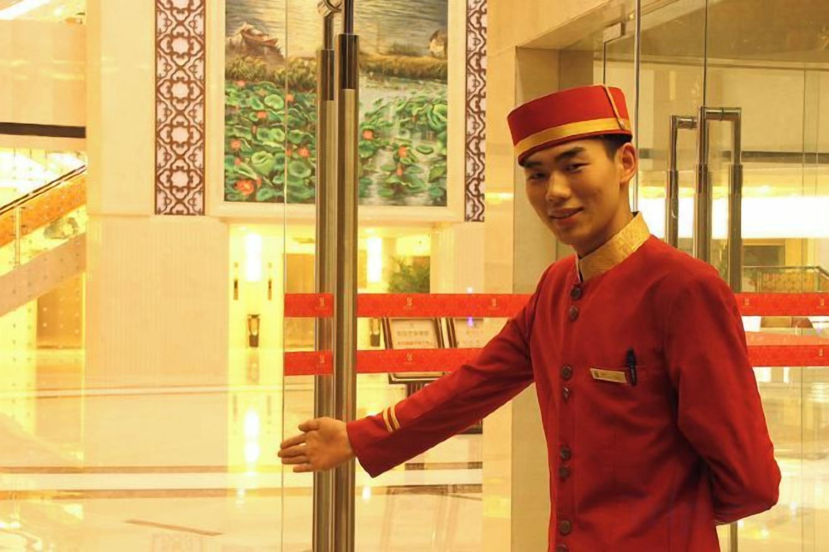 A person in a uniform standing near a glass elevator door in a hotel lobby.
