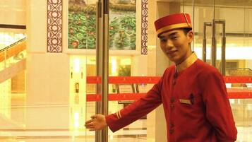 A person in a uniform standing near a glass elevator door in a hotel lobby.