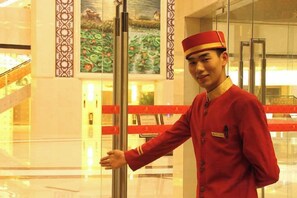 Eine Person in Uniform steht neben einer Glastür eines Aufzugs in der Hotelhalle.