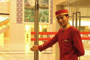 A person in a uniform standing near a glass elevator door in a hotel lobby.