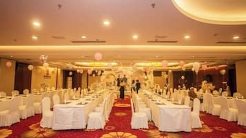 A banquet hall with round tables, white tablecloths, and a red carpet.