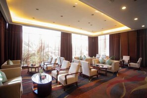A hotel lobby with multiple seating areas, large windows, and a carpeted floor.