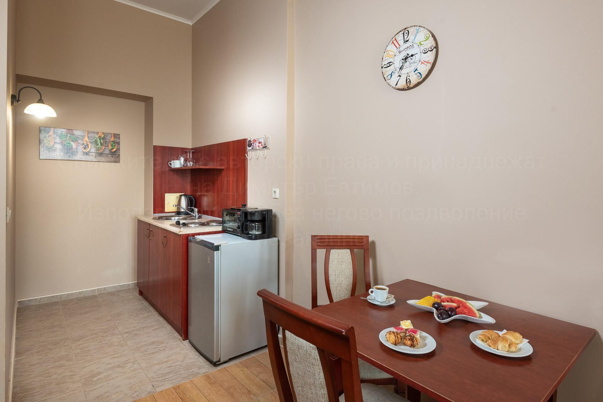 A compact kitchen with a refrigerator, microwave, and coffee maker. A dining table with plates of food and a chair is in the foreground.