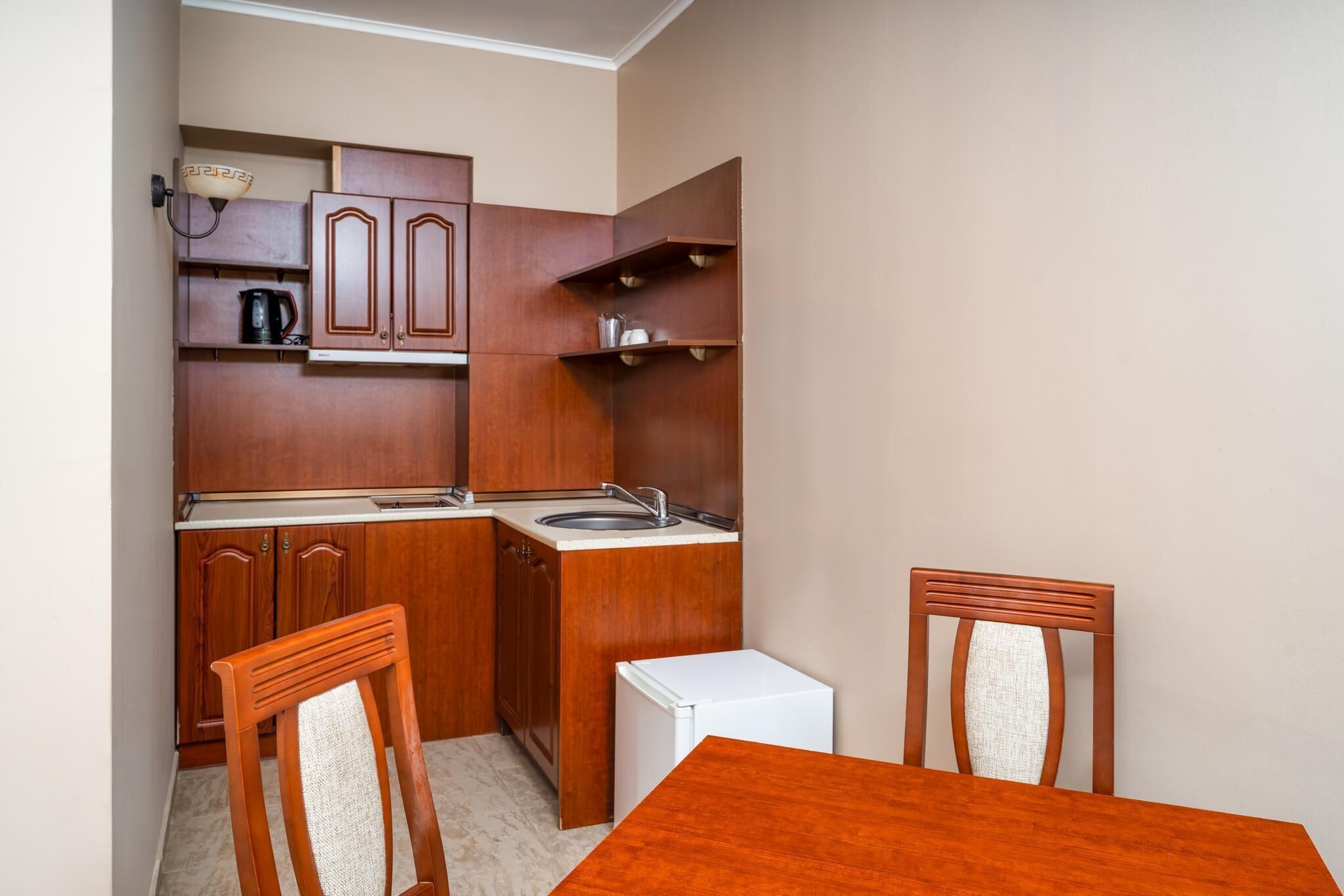 A compact kitchen with wooden cabinets, a white refrigerator, and a dining table with chairs.