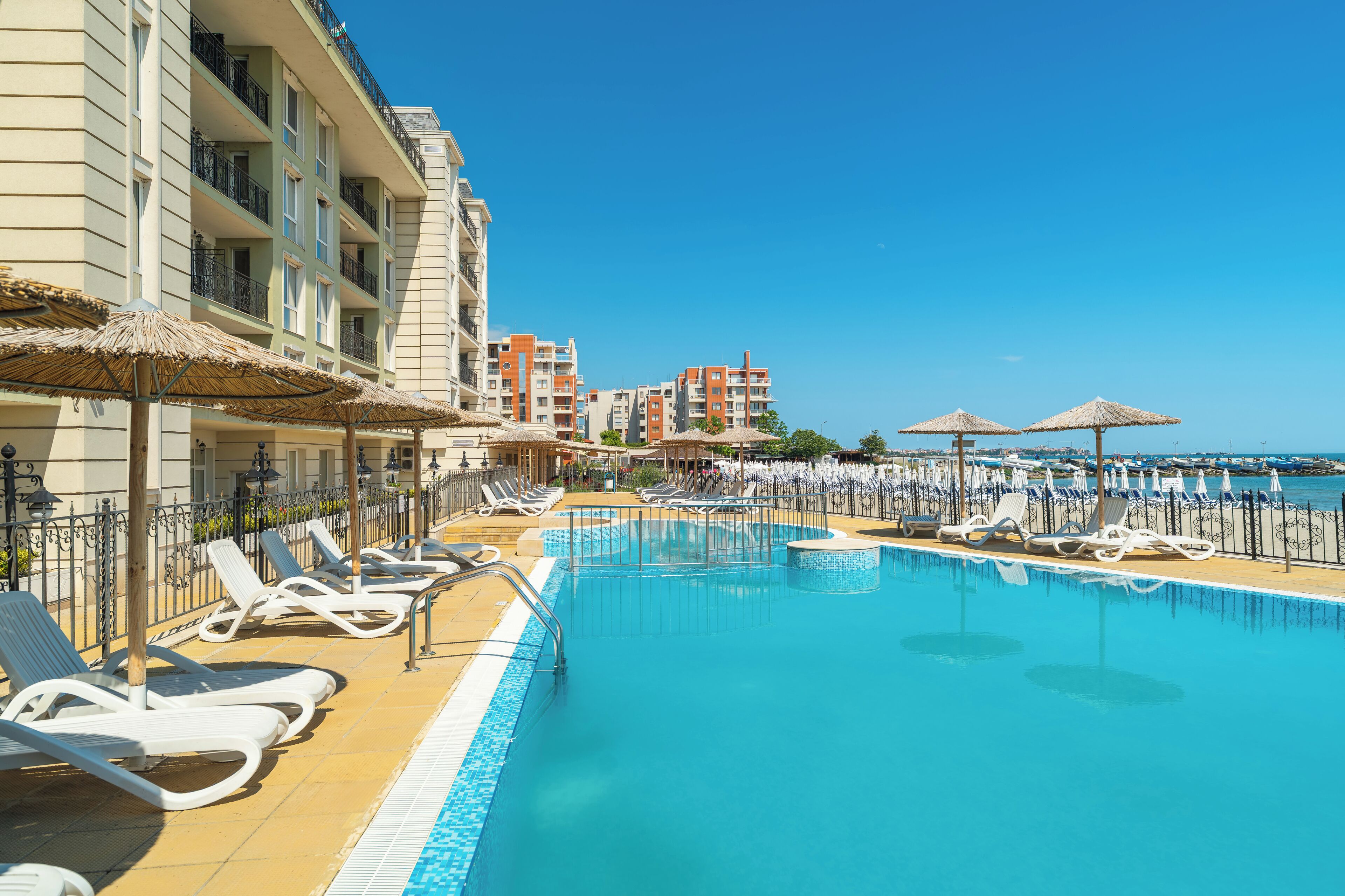 Una piscina con lettini e ombrelloni, circondata da edifici alberghieri con balconi.