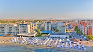 Een resort met meerdere gebouwen, een zwembad en een strand met tal van ligbedden en parasols.