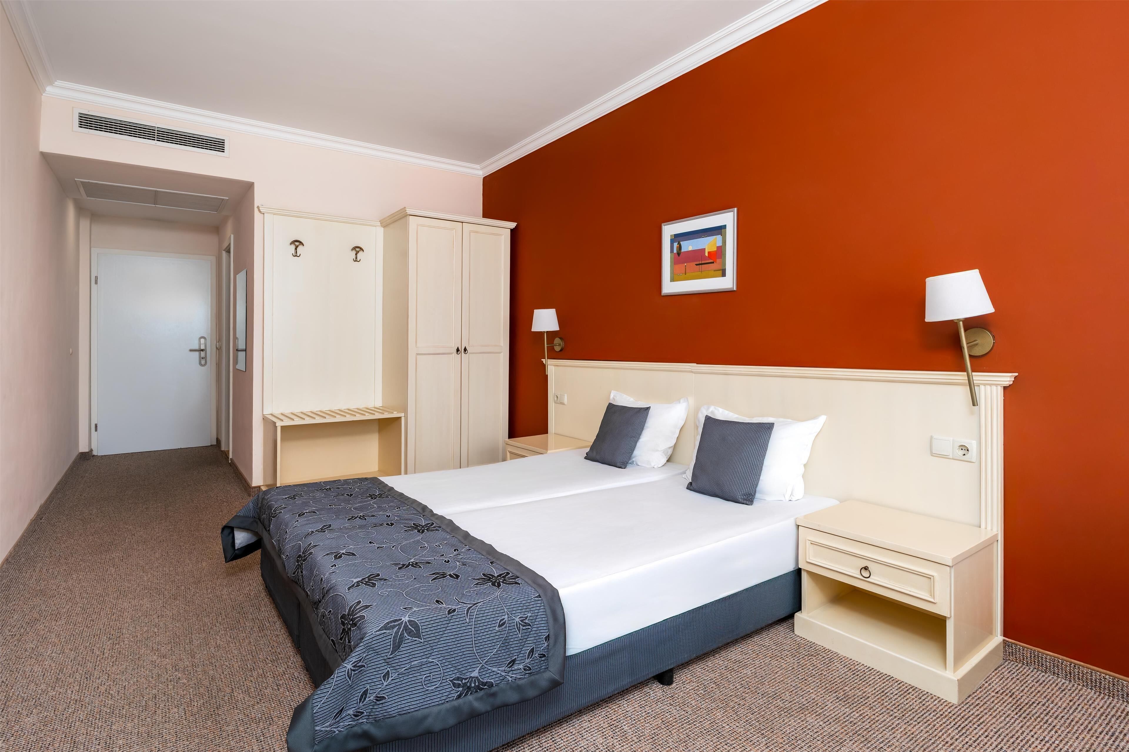 Ein Hotelzimmer mit einem großen Bett, einem Schrank, einem Nachttisch und einer Lampe.
