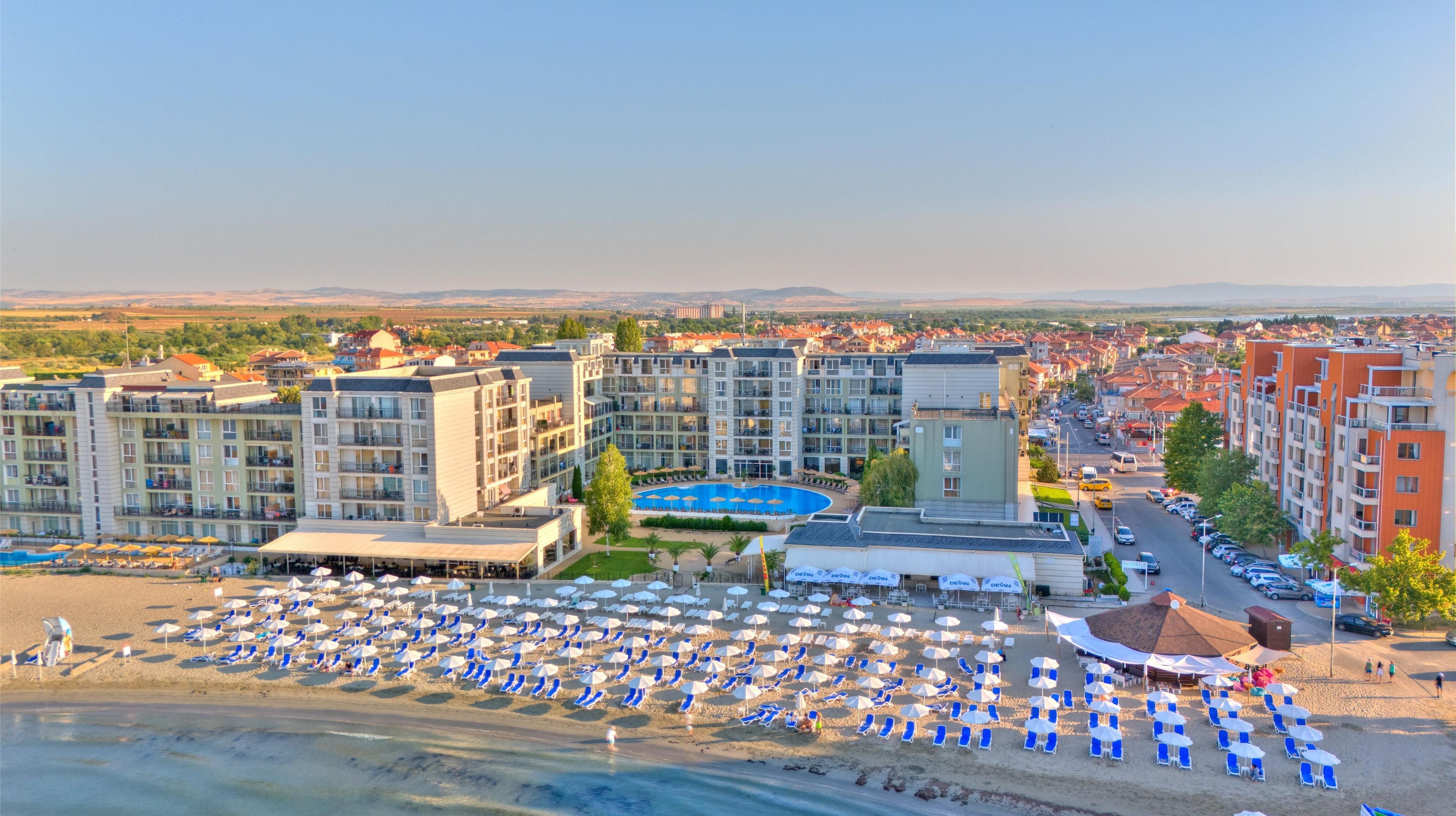 A resort with multiple buildings, a swimming pool, and a beach with numerous sun loungers and umbrellas.