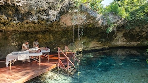 A spa area with wooden platforms and benches overlooking a clear blue pool.