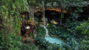 A wooden deck with a table and chairs overlooking a natural pool and waterfall.