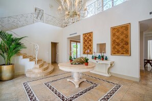 A spacious foyer with a grand staircase, a decorative table, and a large floral painting.