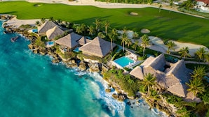 An aerial view of a coastal resort with thatched-roof villas, a swimming pool, and a golf course. - Eden Roc Cap Cana (Punta Cana)