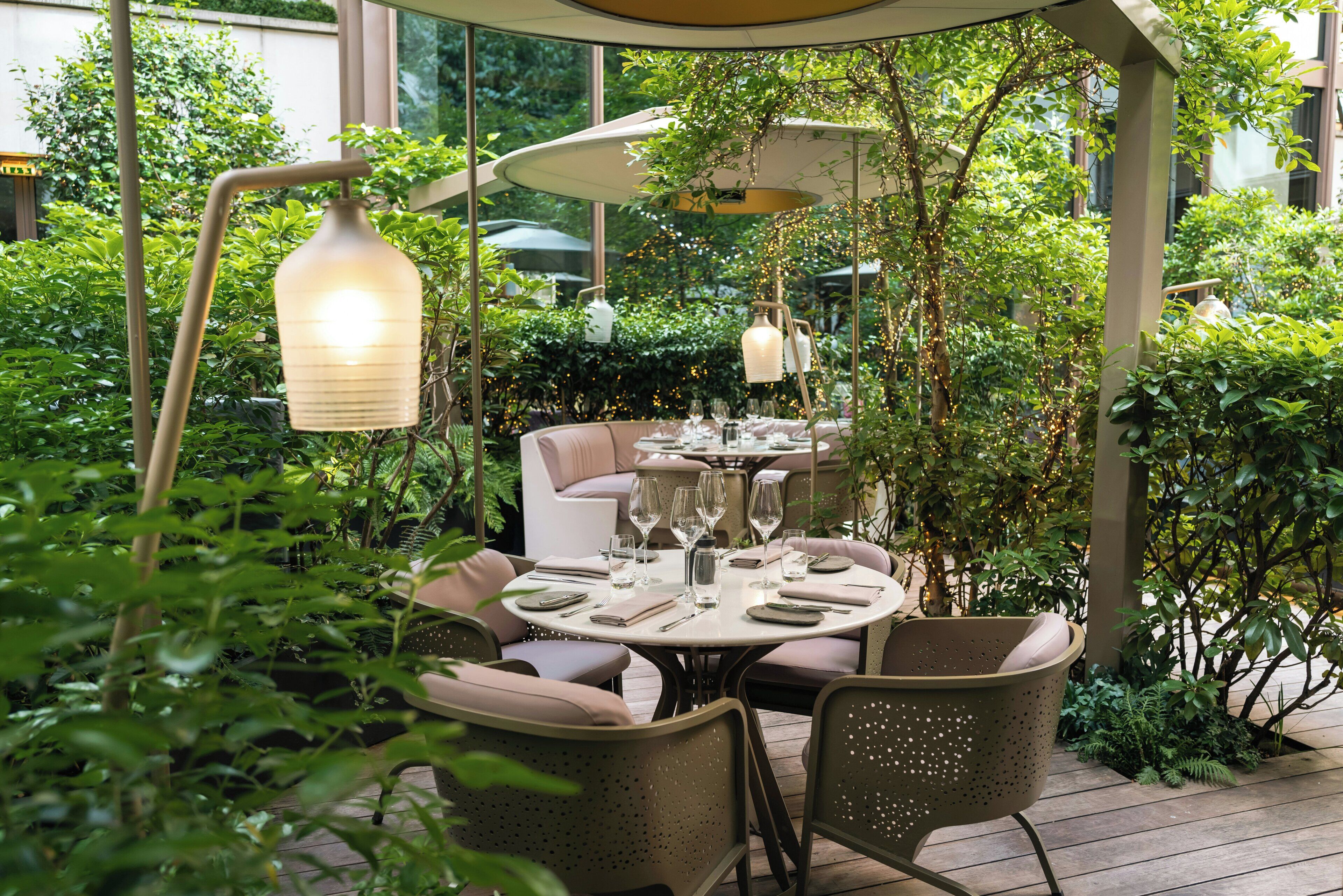 Un espace extérieur aménagé pour les repas, avec des tables rondes, des chaises et des luminaires suspendus.
