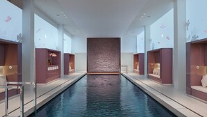 A modern indoor swimming pool with clear water, surrounded by seating areas with built-in benches and tables.