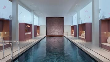 Una piscina interior moderna con agua cristalina, rodeada de zonas de estar con bancos y mesas integrados.