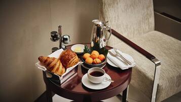 Ein Tisch mit Croissants, Orangen, einer Kaffeetasse und einem Teekessel vor einer beige farbenen Wand mit einem Stuhl.
