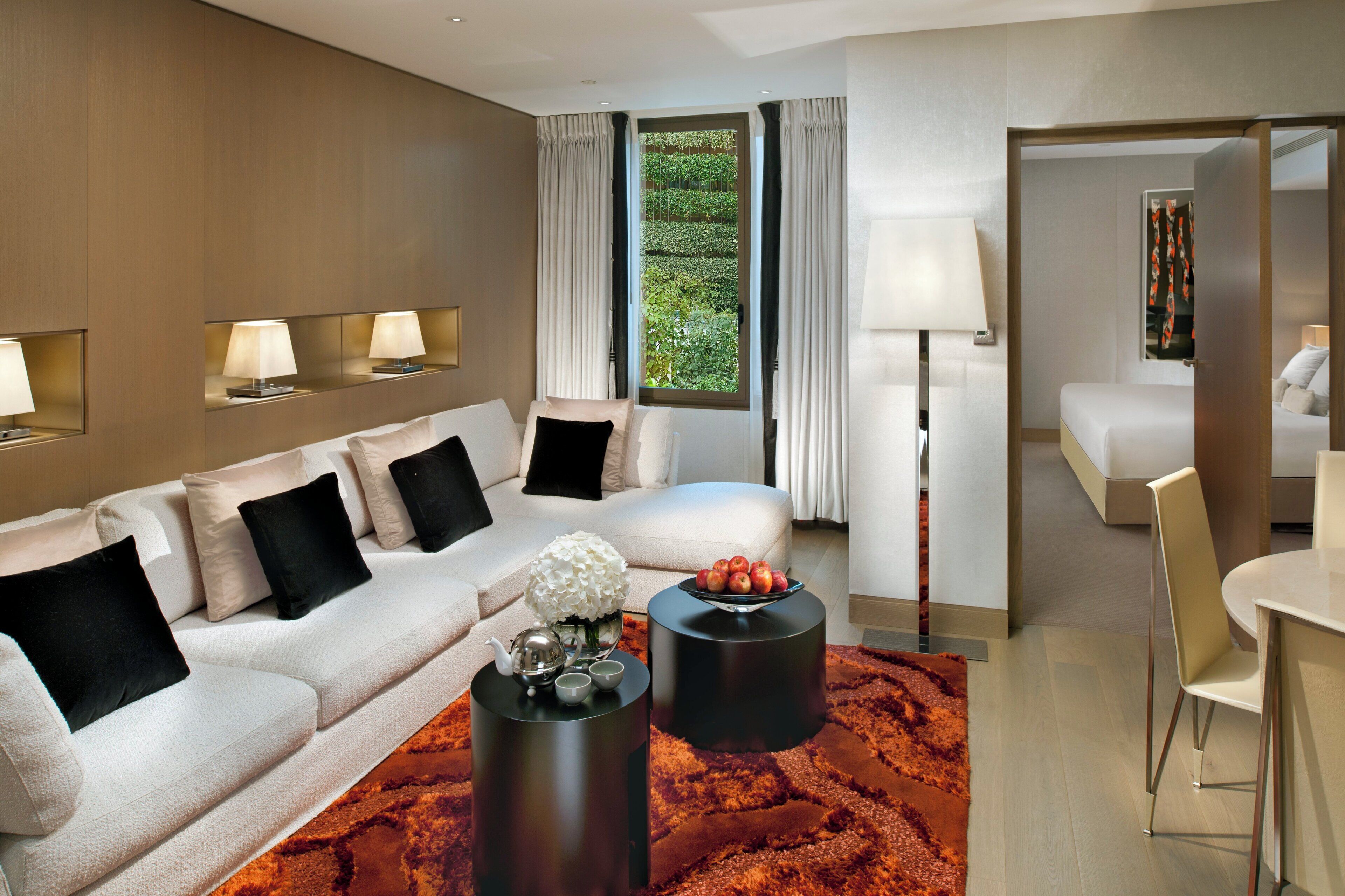 Une chambre d’hôtel moderne, dotée d’un canapé, de deux tables d’appoint, d’un coin repas et offrant une vue sur la verdure par la fenêtre.