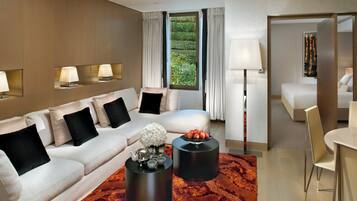 Une chambre d’hôtel moderne, dotée d’un canapé, de deux tables d’appoint, d’un coin repas et offrant une vue sur la verdure par la fenêtre.