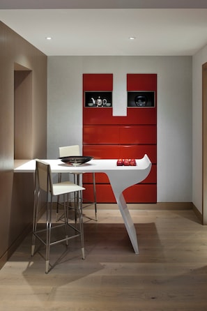 Una cocina moderna con una mesa blanca y armarios rojos, una silla blanca y un lavamanos de acero inoxidable.