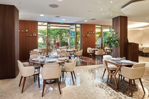 A hotel dining area with multiple tables and chairs, large windows offering a view of the outdoors, and a polished floor. - Mandarin Oriental, Paris (Paris)