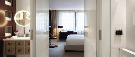 Habitación de hotel con cama, escritorio, espejo y baño con ducha.