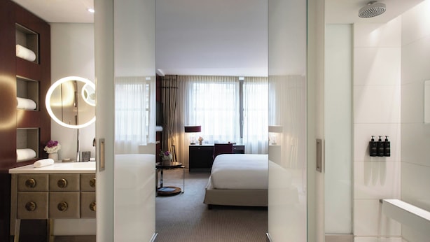 A hotel room with a bed, a desk, a mirror, and a bathroom with a shower.