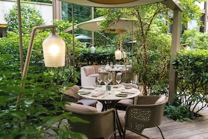 Un espacio al aire libre para comer, con mesas redondas, sillas y lámparas colgantes.