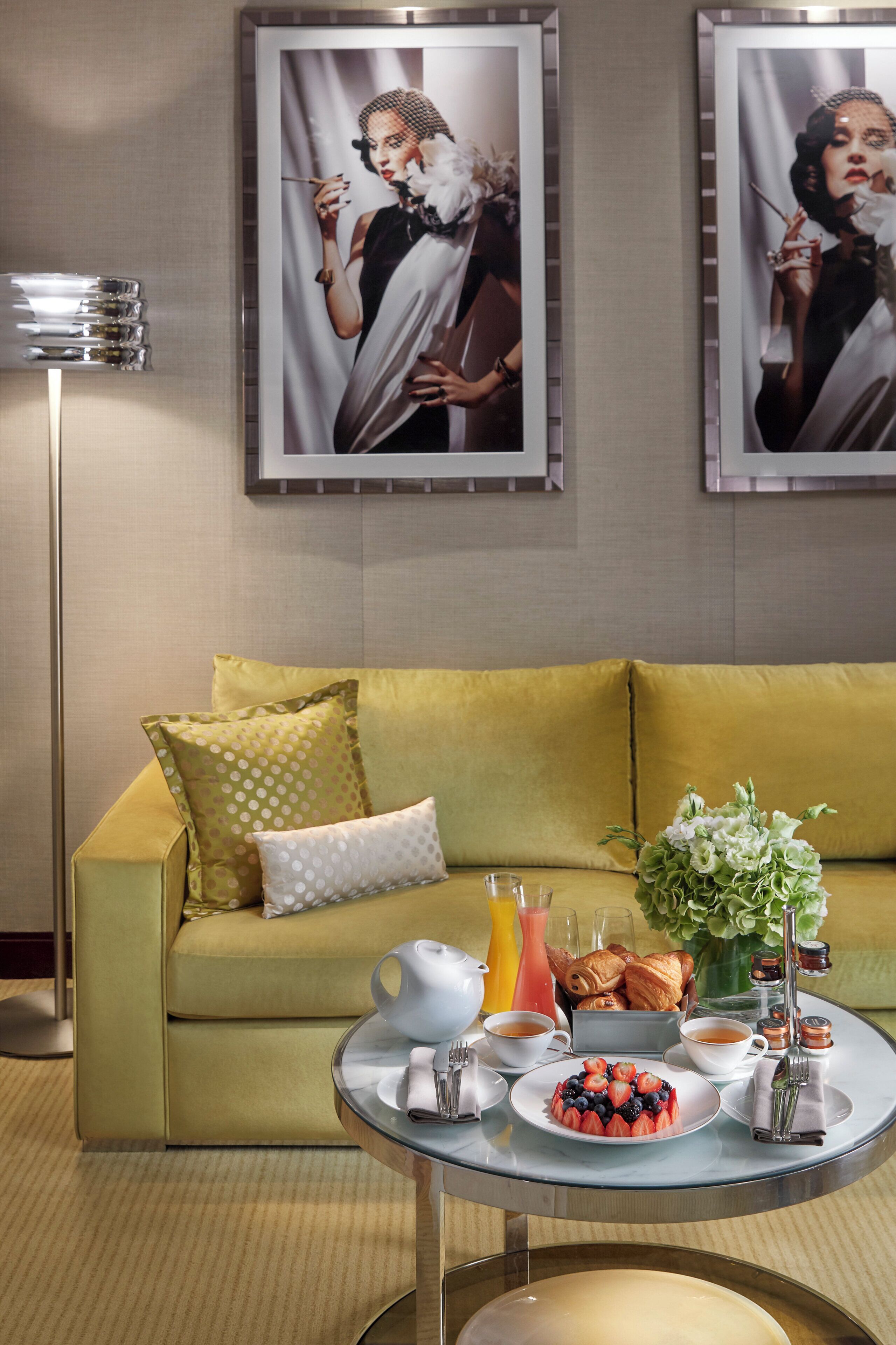 A room with a green sofa, a coffee table with breakfast items, and two framed pictures on the wall.