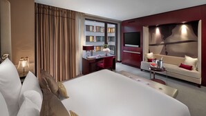 Una habitación de hotel moderna con una cama grande, un escritorio con computadora, un televisor y un área de descanso con un sofá y una mesita.
